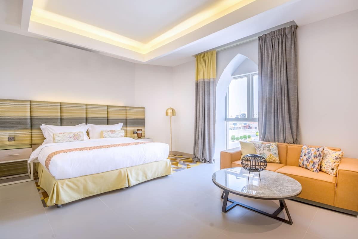 Una habitación de hotel con cama, sofá, mesa de centro y un ventanal con cortinas.