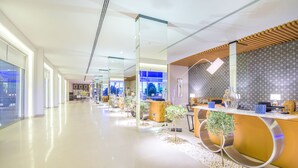 Moderni hotellin aula, jossa on vastaanottotiski, oleskelualueita ja lasiseinä, josta avautuu näkymä ulos.