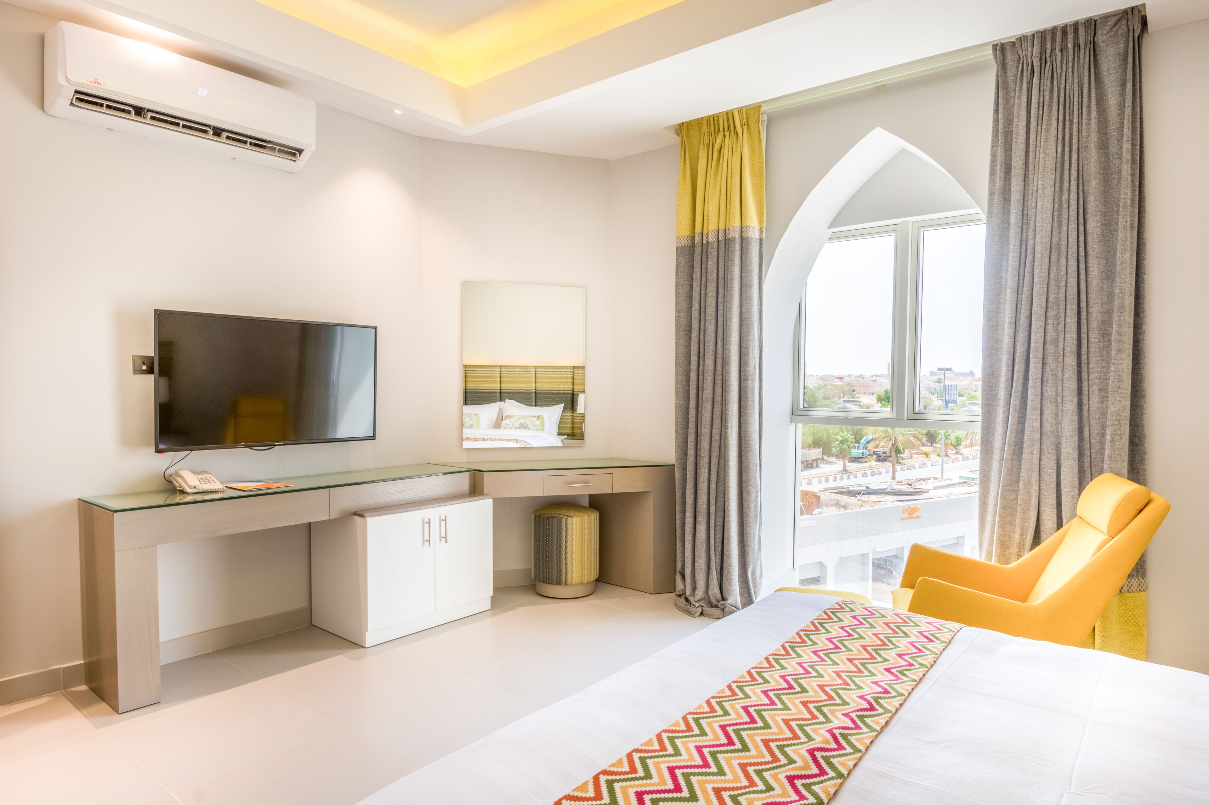 Une chambre d’hôtel moderne dotée d’un grand lit, d’un bureau avec un téléviseur à écran plat, d’une chaise et d’une fenêtre avec des rideaux.