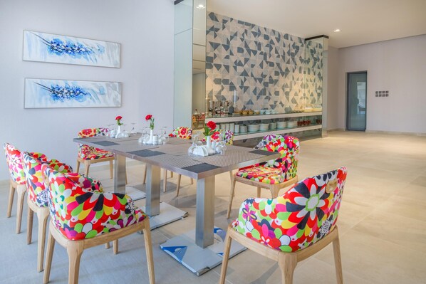 A dining area with a long table, colorful chairs, and a patterned wall in the background.