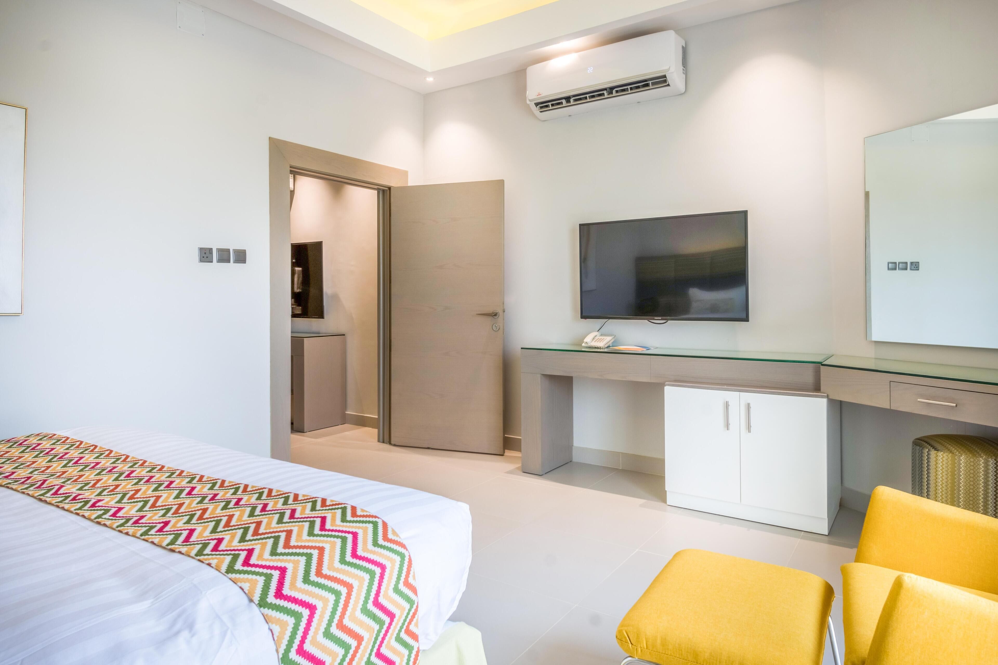 Quarto de hotel moderno com cama, escrivaninha, televisão e guarda-roupa.