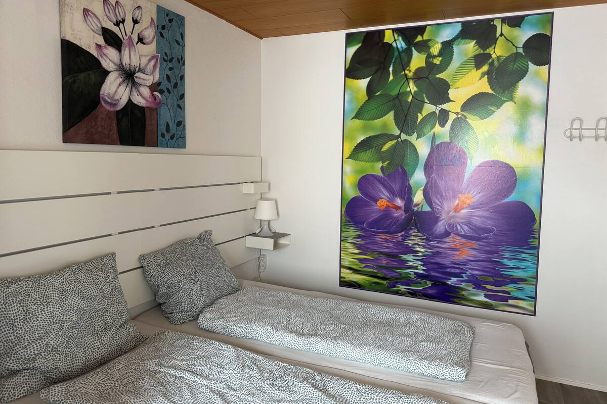 A bedroom with a bed, a nightstand, a lamp, and two paintings on the wall.