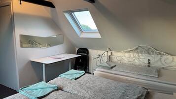 A bedroom with a sloped ceiling, a skylight, a bed with patterned bedding, a desk with a chair, and a radiator.