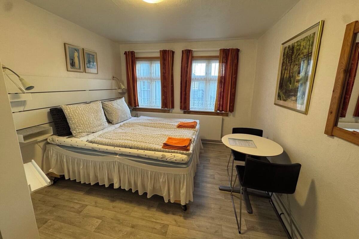 A hotel room with a bed, a desk, and a chair. There are two windows with curtains.