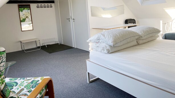 A bedroom with a bed, a desk, a chair, a window, and a door.
