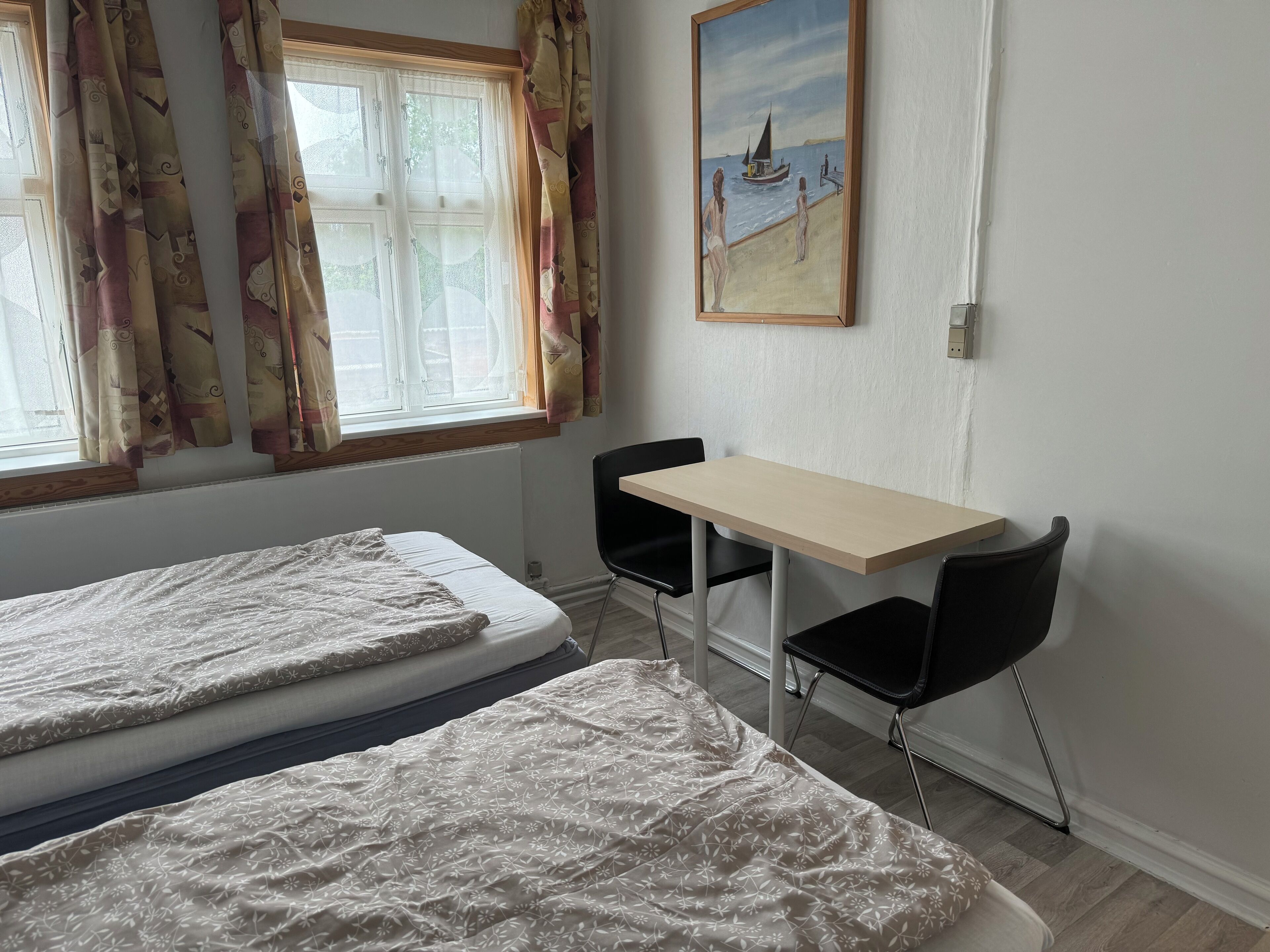 Quarto com duas camas, uma escrivaninha e cadeiras.