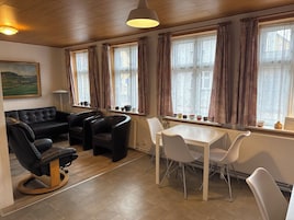 Una sala de estar con un sofá de cuero negro, dos sillones de cuero negro, una mesa de comedor blanca con cuatro sillas y un cuadro en la pared.