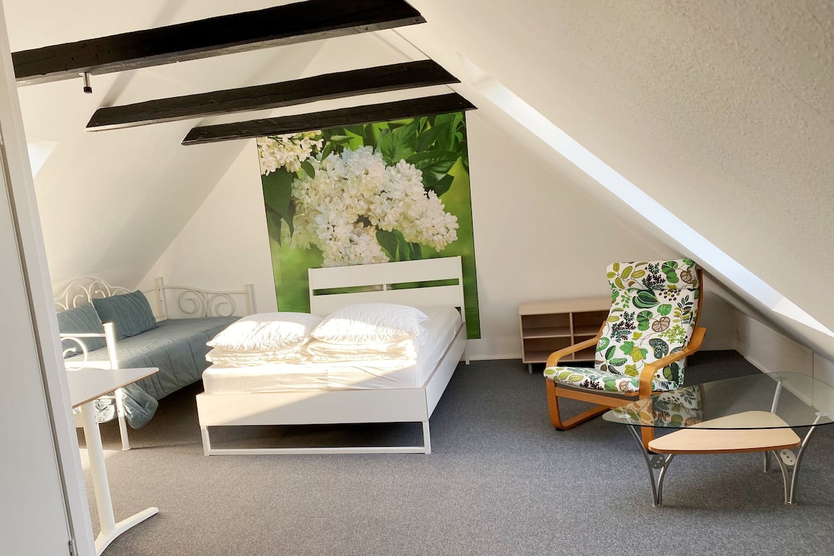 A cozy attic bedroom with a bed, a chair, and a green wall mural.