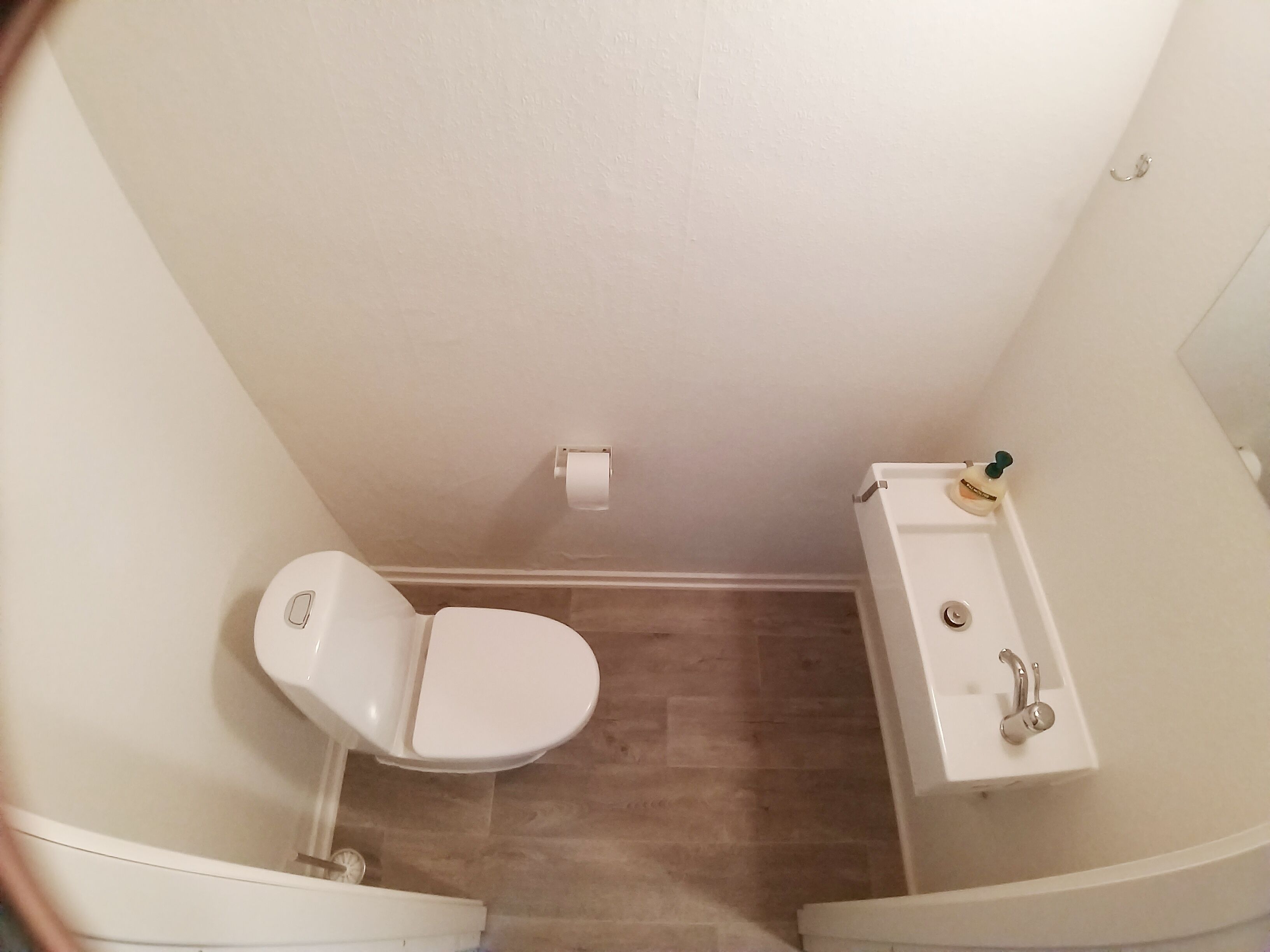 A small bathroom with a toilet, sink, and a bottle of hand soap.