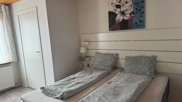 Una stanza con due letti singoli, un comodino con una lampada, un quadro appeso al muro e una finestra con tende.
