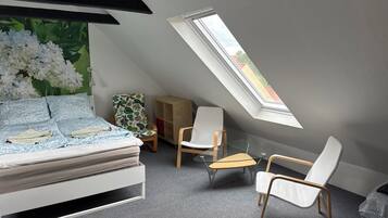 Une chambre à coucher comprenant un lit, une chaise, une petite table, une bibliothèque et une lucarne.