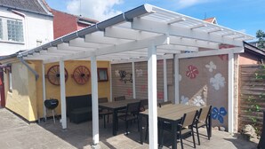 A covered patio area with tables and chairs, a barbecue grill, and decorative wall art.
