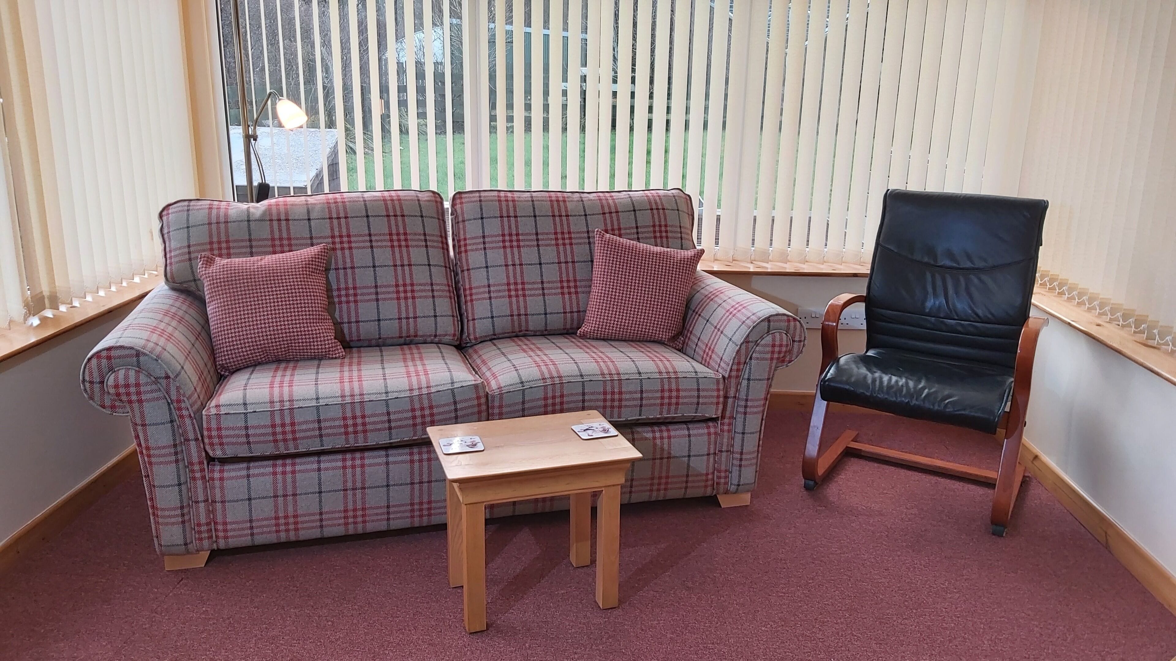 A living room with a plaid sofa, a wooden coffee table, and a black leather chair.