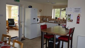 A compact kitchen with a refrigerator, microwave, and sink. There is a dining table with four chairs, and a fire extinguisher mounted on the wall. - Roe Deer Cottage (Beauly)