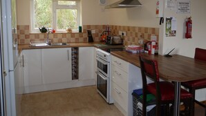 A kitchen with white cabinets, a sink, a stove, and a window with blinds. There is a fire extinguisher on the wall and a sign with a phone number. - Roe Deer Cottage (Beauly)