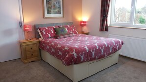 A bedroom with a bed, two bedside tables, a nightstand, a radiator, and a window with curtains. - Roe Deer Cottage (Beauly)