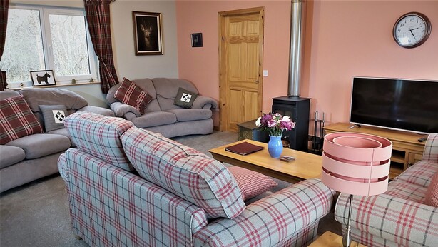 A cozy living room with two sofas, a coffee table, a TV, a fireplace, and a clock on the wall. - Roe Deer Cottage (Beauly)