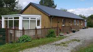 A wooden building with a covered porch and a gravel driveway. - Roe Deer Cottage (Beauly)