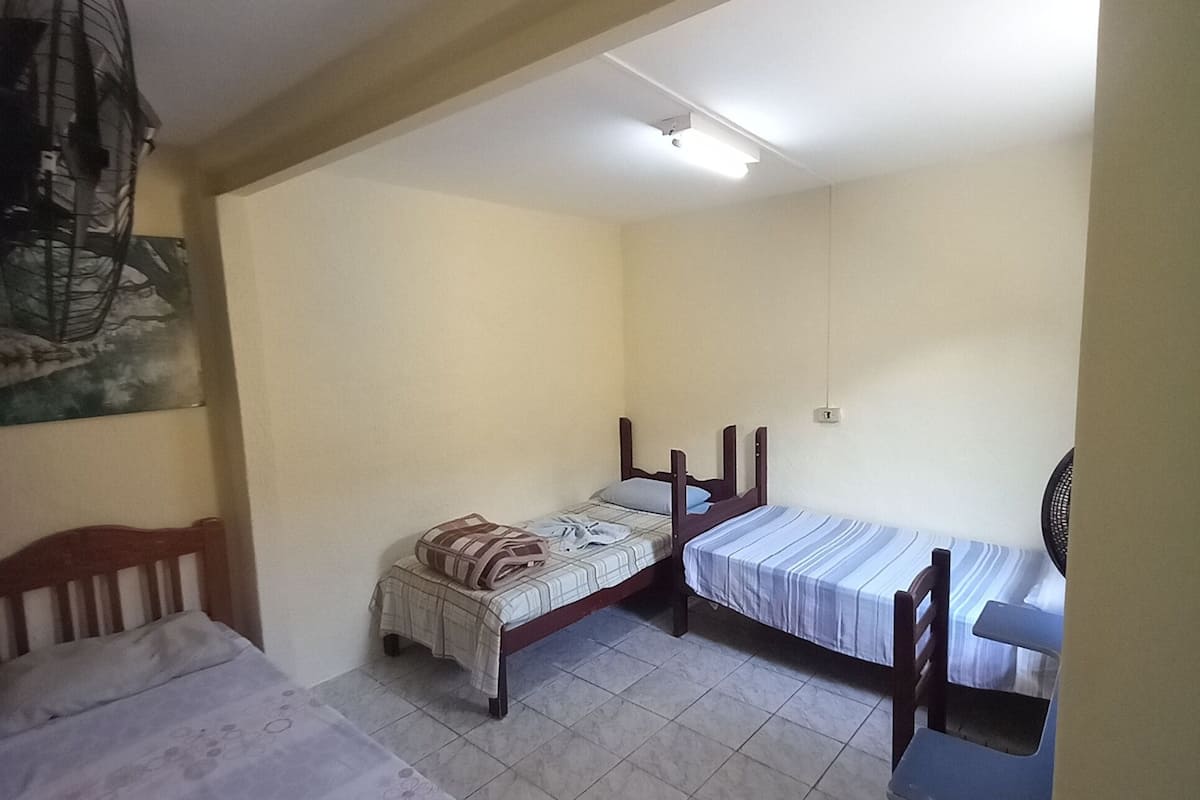 A dormitory room with two single beds, a chair, a fan, and a ceiling fan.