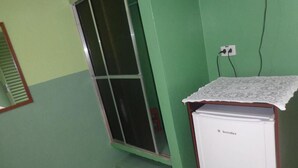 Una habitación pequeña con una pared verde, una ventana con marco de metal, un refrigerador blanco y un enchufe en la pared.