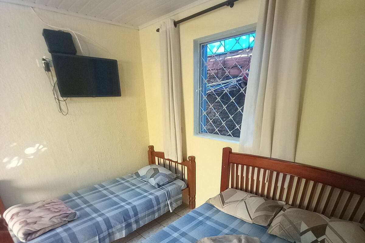 A room with two beds, a ceiling fan, a window with curtains, and a mounted TV.