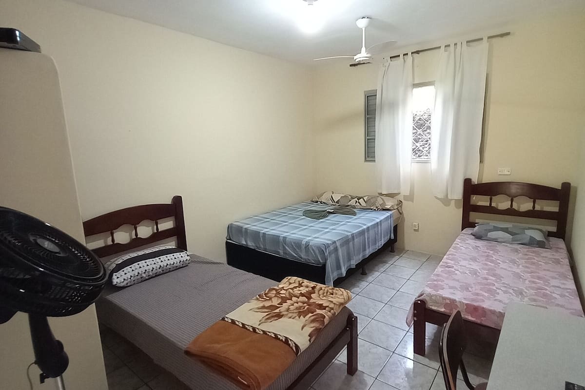 A small, clean room with two beds, a desk, and a ceiling fan.