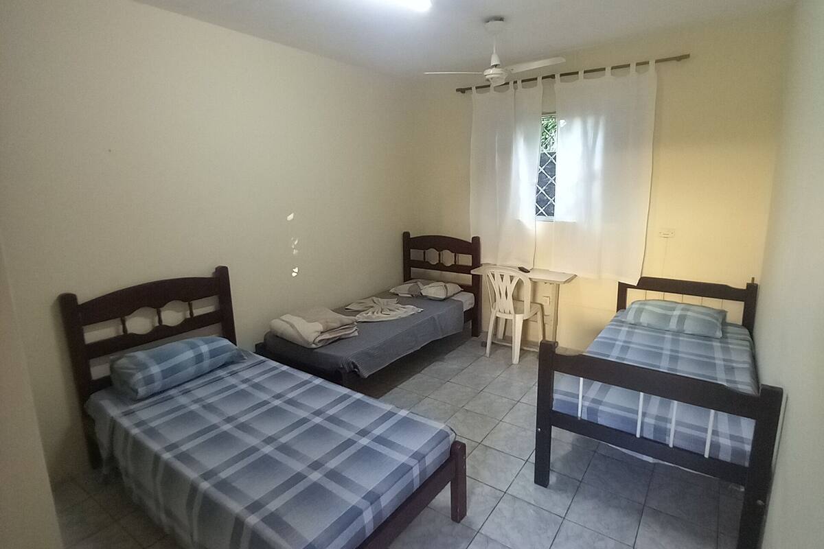 A room with three beds, a ceiling fan, and a window with curtains.