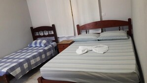 Una habitación pequeña y limpia con dos camas individuales, un cabecero de madera, una mesita de noche y una toalla blanca sobre la cama más grande.