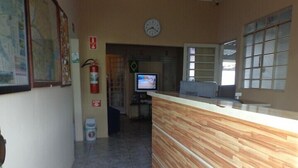 Zona de recepción con un mostrador de madera, un reloj en la pared y una pantalla de televisión.
