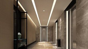 Un couloir moderne avec un sol en marbre, une cloison en verre et un ascenseur au design minimaliste.
