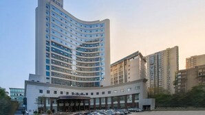 Un hôtel moderne à la façade incurvée, doté de plusieurs étages et d’un espace d’entrée abrité, avec un parking situé devant.