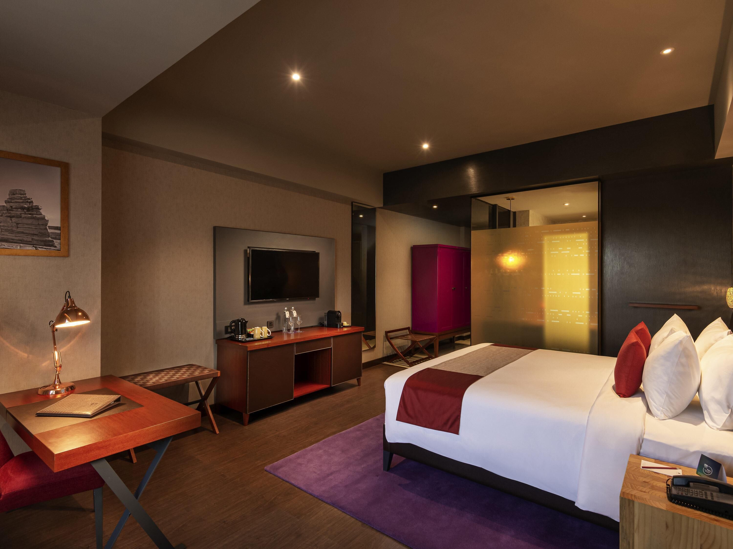 A hotel room with a bed, desk, chair, TV, and a red cabinet.