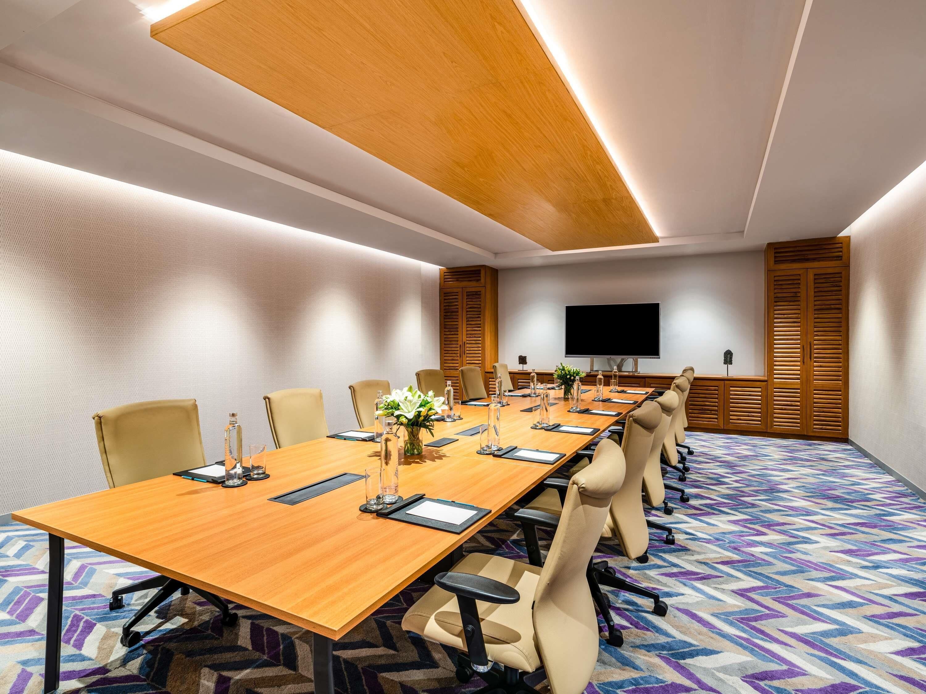 Une salle de conférence avec une longue table, des chaises, un téléviseur à écran plat et une moquette à motifs.