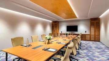 A conference room with a long table, chairs, a flat-screen TV, and a patterned carpet.