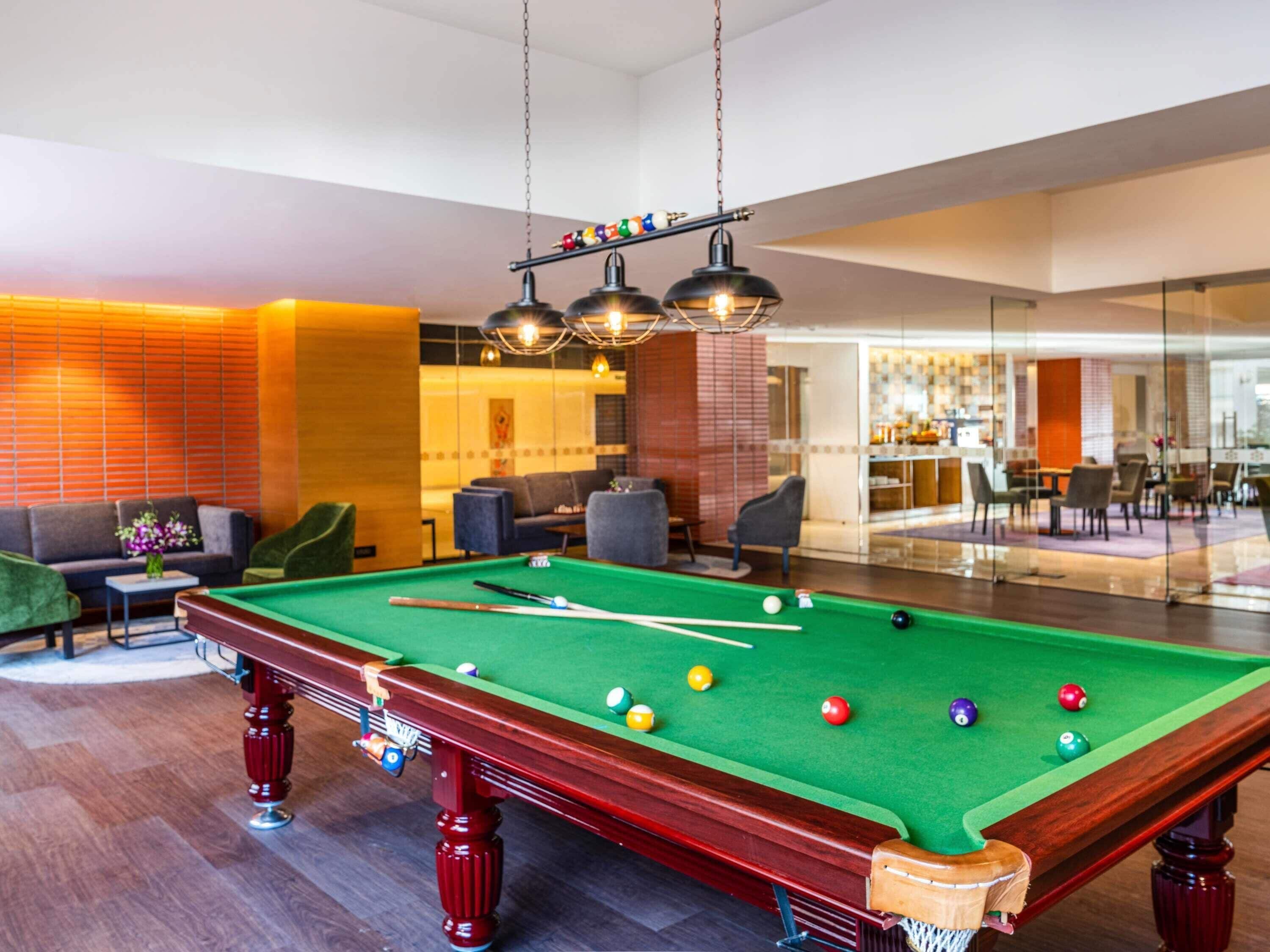 A pool table in a modern room with a sofa and chairs, a dining area in the background, and a bar.