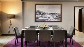 A dining area with a table set for four, a large framed picture on the wall, and a floor lamp.