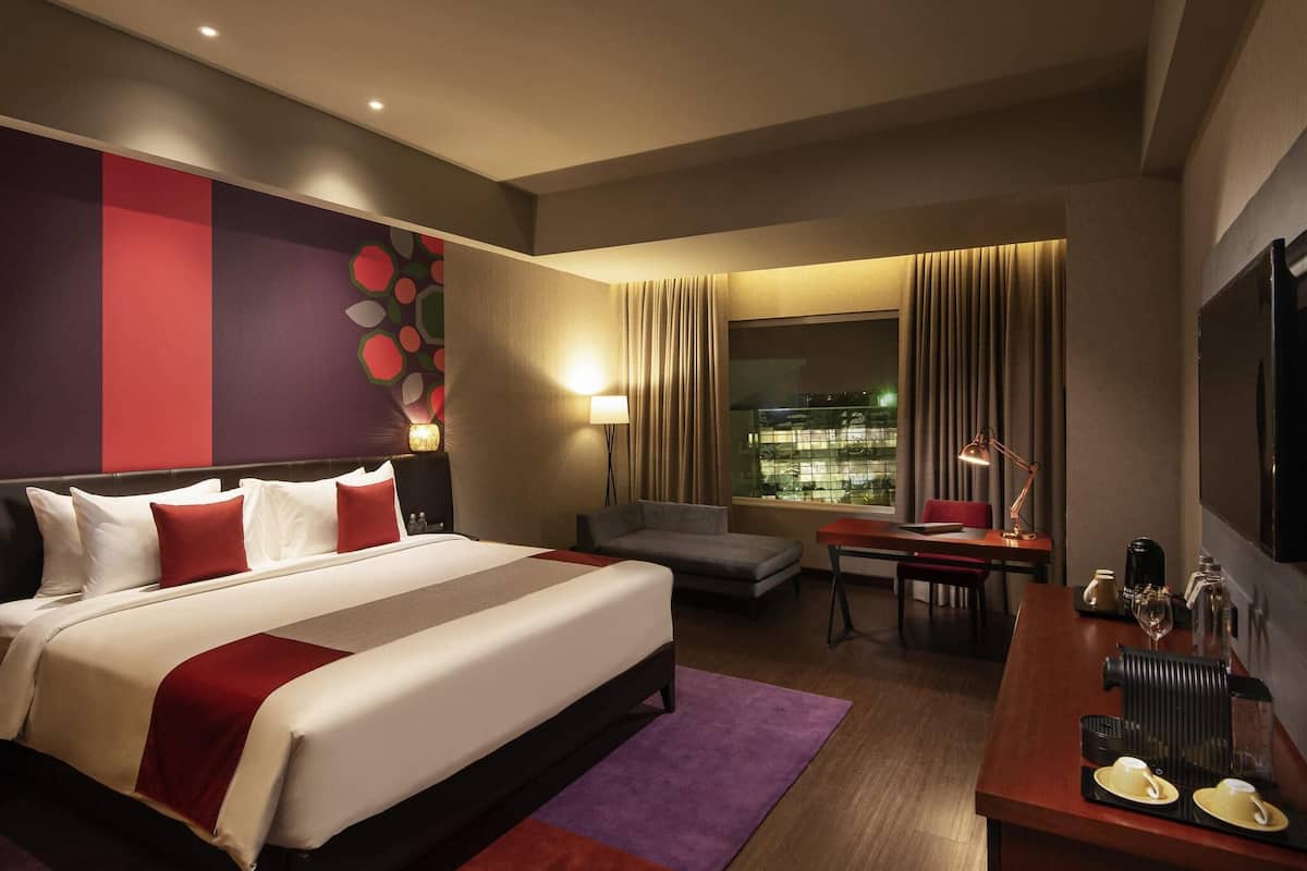 Ein Hotelzimmer mit Bett, Schreibtisch, Stuhl, Fernseher und einem Fenster mit Vorhängen.