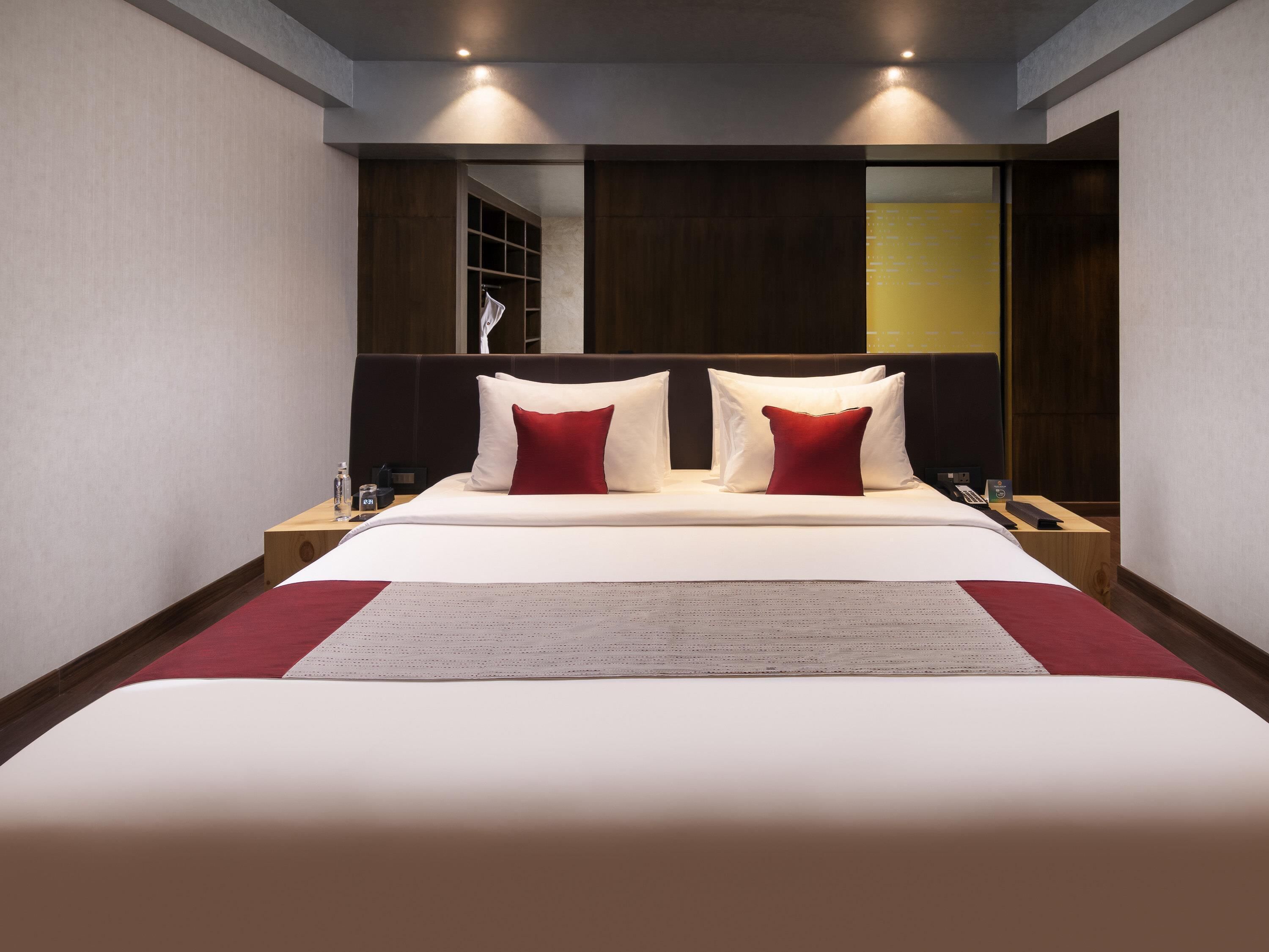 A hotel room with a large bed, two bedside tables, a nightstand, a mirror, and a wardrobe.