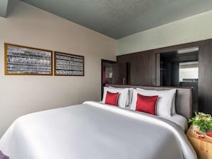 Habitación de hotel con una cama grande, dos cuadros enmarcados en la pared, un cabecero de madera y una mesita de noche con una planta.