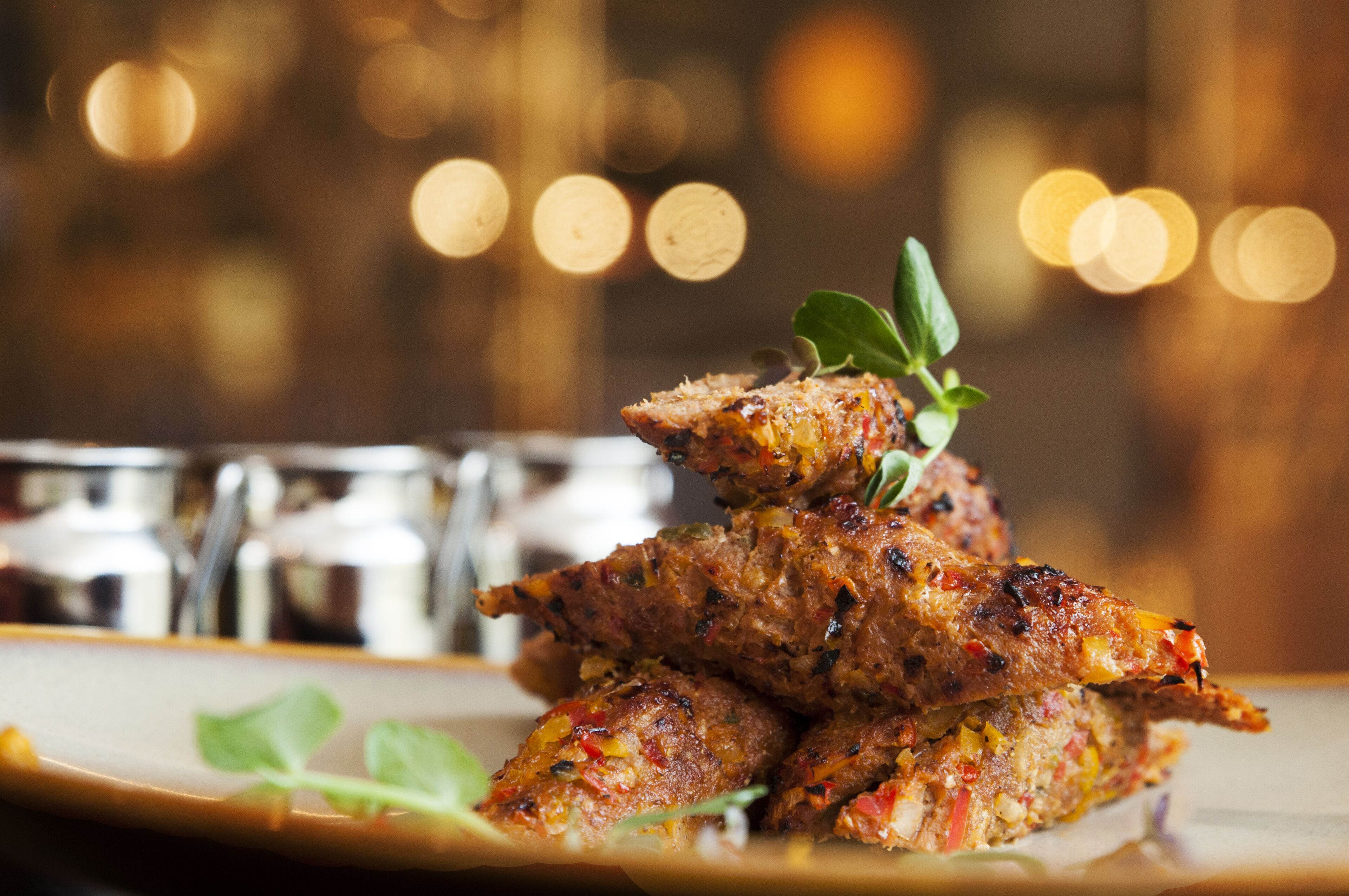 A plate of grilled meat garnished with a leaf, with blurred background lights.