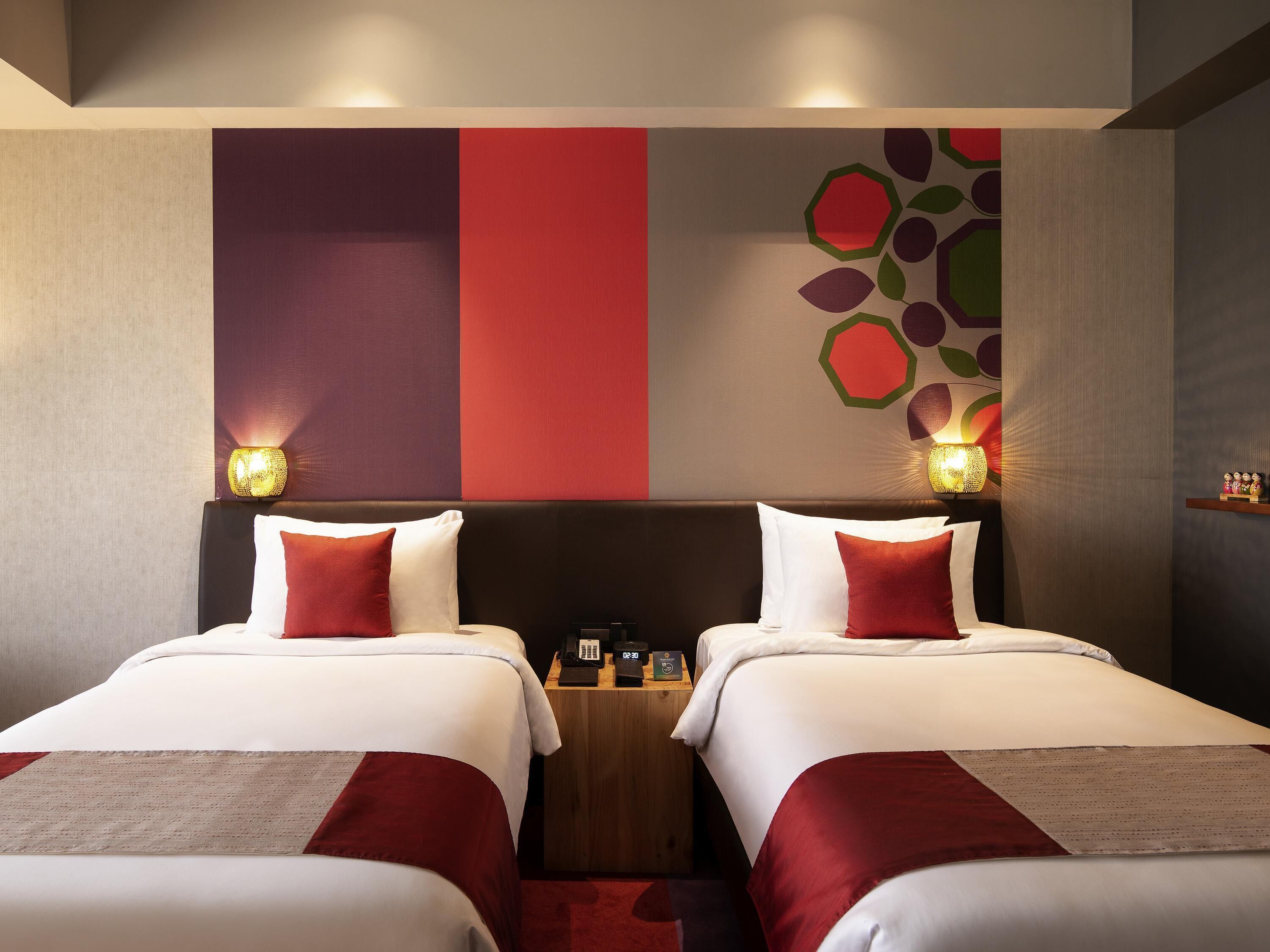 A hotel room with two beds, a wooden nightstand, and a wall with a geometric design.