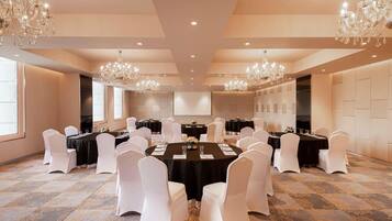 A conference room with round tables, white chairs, chandeliers, and a carpeted floor.