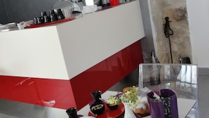 A modern kitchen with a red and white color scheme, featuring a countertop with various kitchen appliances and a glass dining table set with plates, bowls, and a vase. - B&B Terra Marique (Syracuse)