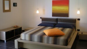 A modern bedroom with a large bed, a bedside table, a nightstand, a cabinet, and a wall-mounted air conditioner. - B&B Terra Marique (Syracuse)