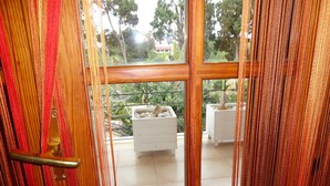 A view through a wooden-framed window with a metal handle, leading to an outdoor area with white furniture and a white planter. - B&B Terra Marique (Syracuse)