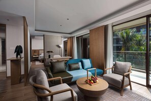 Una habitación de hotel moderna con sofá, sillas, una mesita de centro y un amplio ventanal con vistas a palmeras.