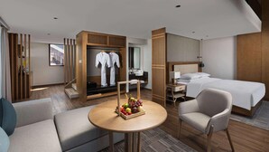 A hotel room with a bed, a desk, a chair, a sofa, a wardrobe, and a table with fruit. - Wingate by Wyndham Hainan Chengmai (Chengmai)