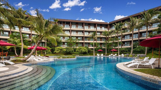 A hotel with a swimming pool, palm trees, and red umbrellas. - Wingate by Wyndham Hainan Chengmai (Chengmai)