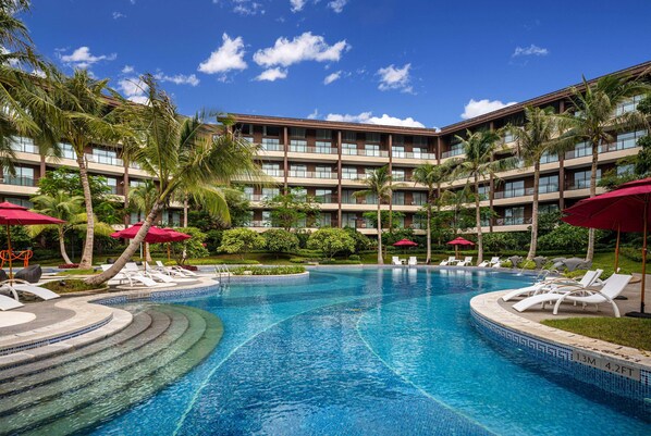 Un hotel con piscina, palmeras y sombrillas rojas.