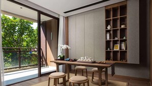 A modern interior with a wooden table, stools, a bookshelf, and a view of greenery outside. - Wingate by Wyndham Hainan Chengmai (Chengmai)